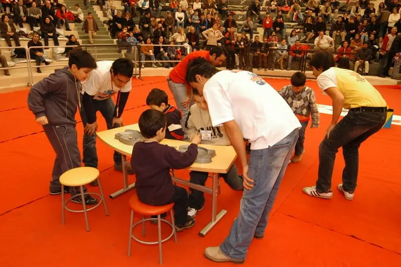 Salondaki Beyblade turnuvasında masa başında yarışan çocuklar